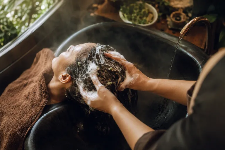 Client relaxing at dark ceramic shampoo basin during soothing botanical treatment